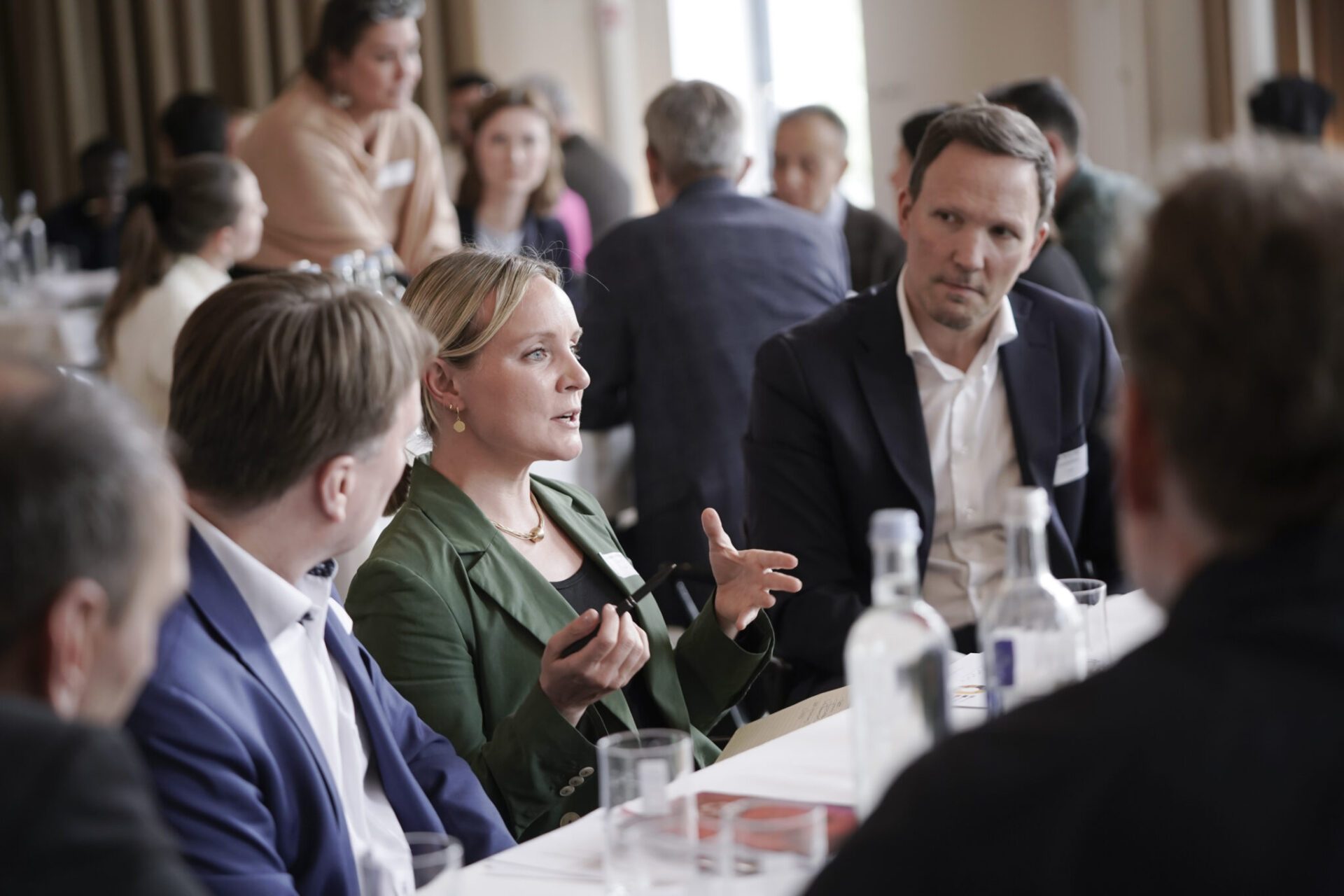 Eine Frau sitzt zwischen vielen weiteren Menschen und redet gestikulierend.