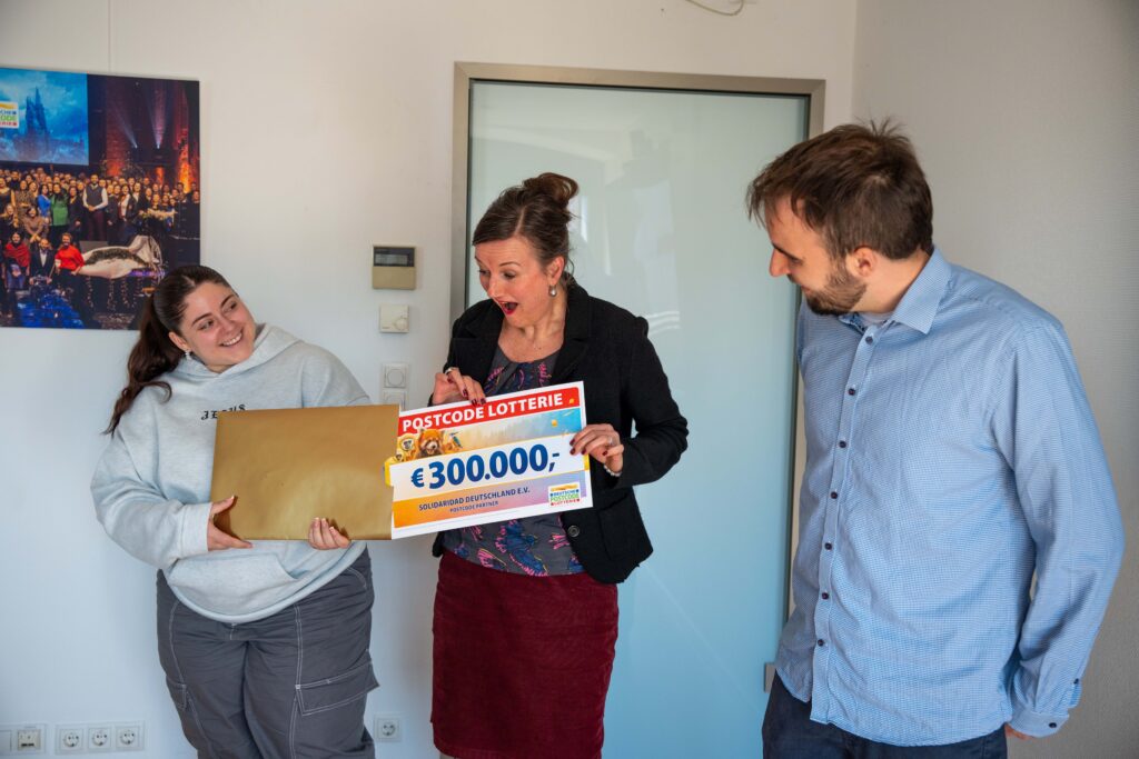 Vertreterin von Solidaridad Deutschland reagiert überrascht und erfreut beim Erhalt des symbolischen 300.000-Euro-Schecks der Postcode Lotterie.