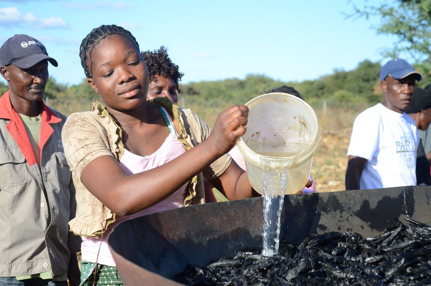 Eine sambische Frau schüttet Wasser über heiße Pflanzenkohle, um sie abzukühlen – Teil eines Trainings zur Verbesserung der Bodenfruchtbarkeit im Solidaridad-Projekt.