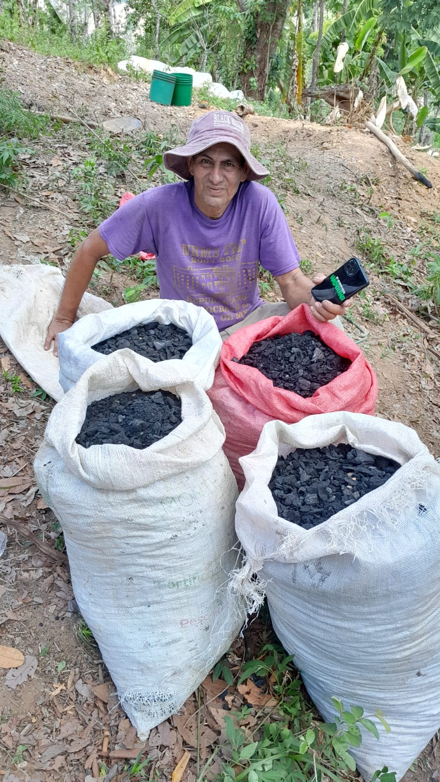 Kakaobauer Don Toñito aus Nicaragua sitzt stolz neben vier großen Säcken, die bis zum Rand mit Pflanzenkohle (Biochar) gefüllt sind, welche handwerklich aus Kakaoresten hergestellt wurde.